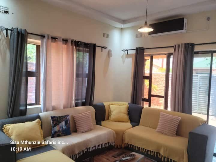 Bright open-plan lounge with a large corner couch at Granadilla Cottage, Victoria Falls